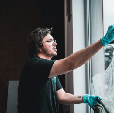 Ein professioneller Fensterreiniger reinigt eine Glasfassade eines Bürogebäudes in Bochum bei sonnigem Wetter.